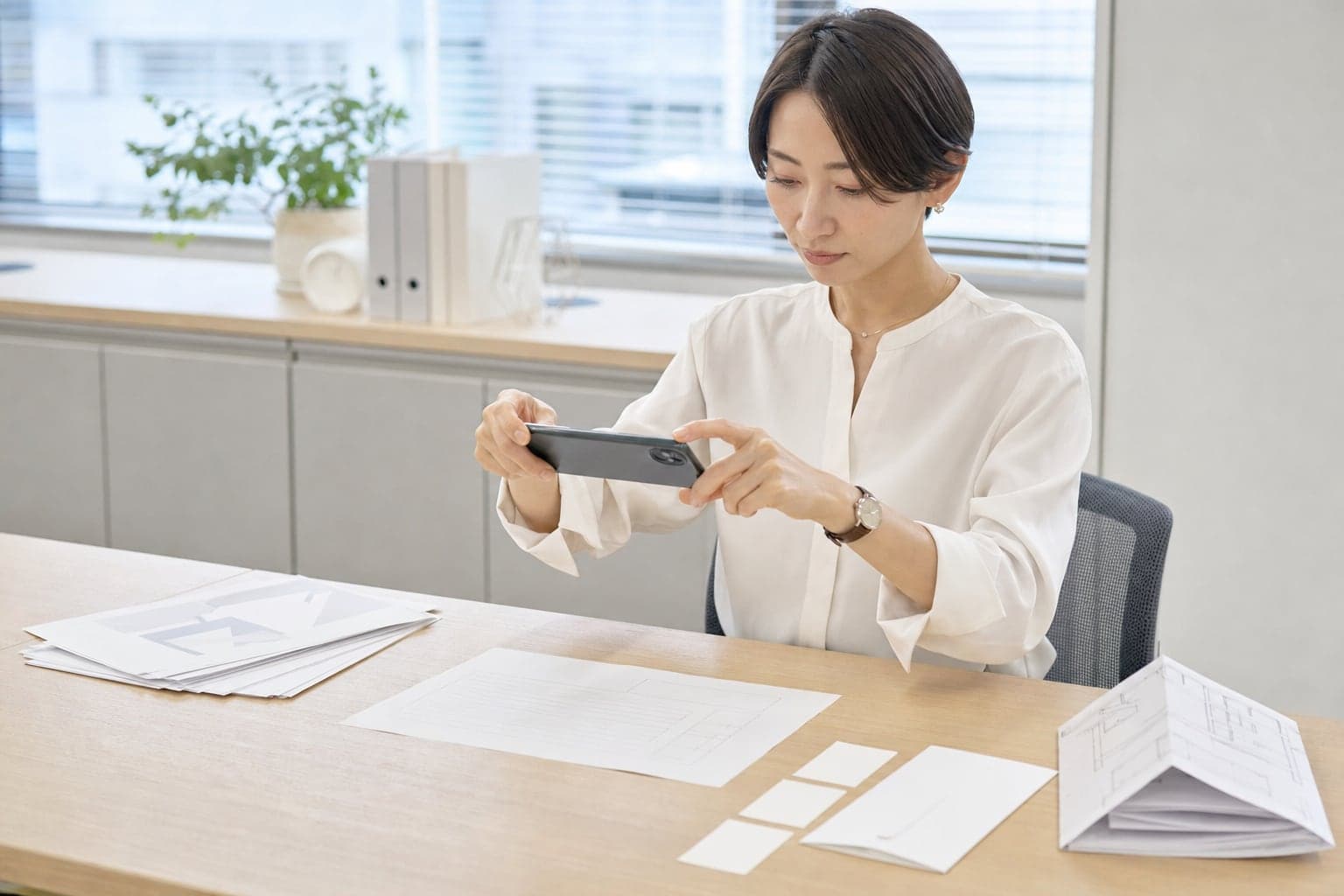 オフィスの机で、スマートフォンを書類にかざして撮影している担当者